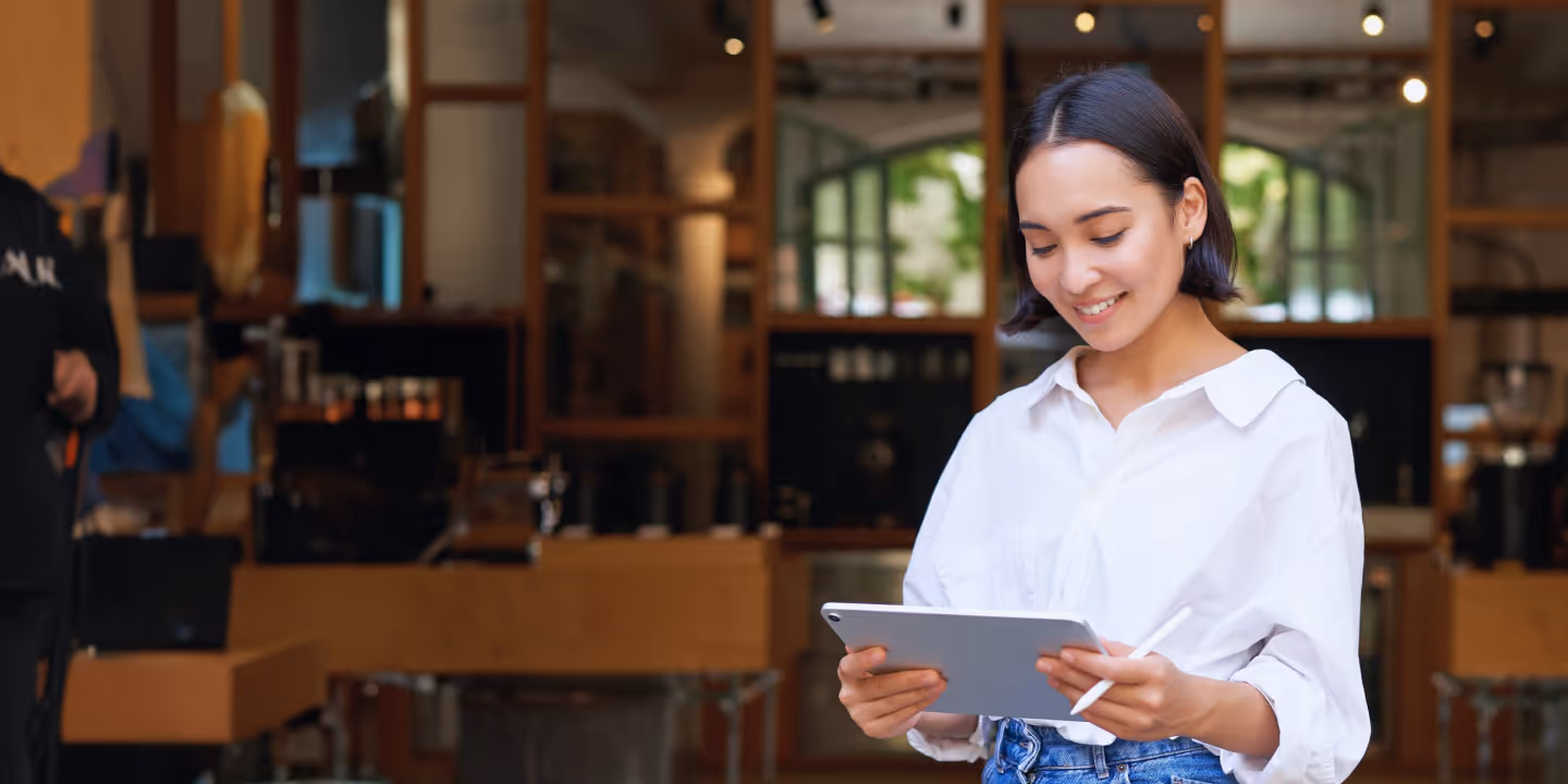 Smiling woman using a digital tablet with a stylus inside a modern café.
